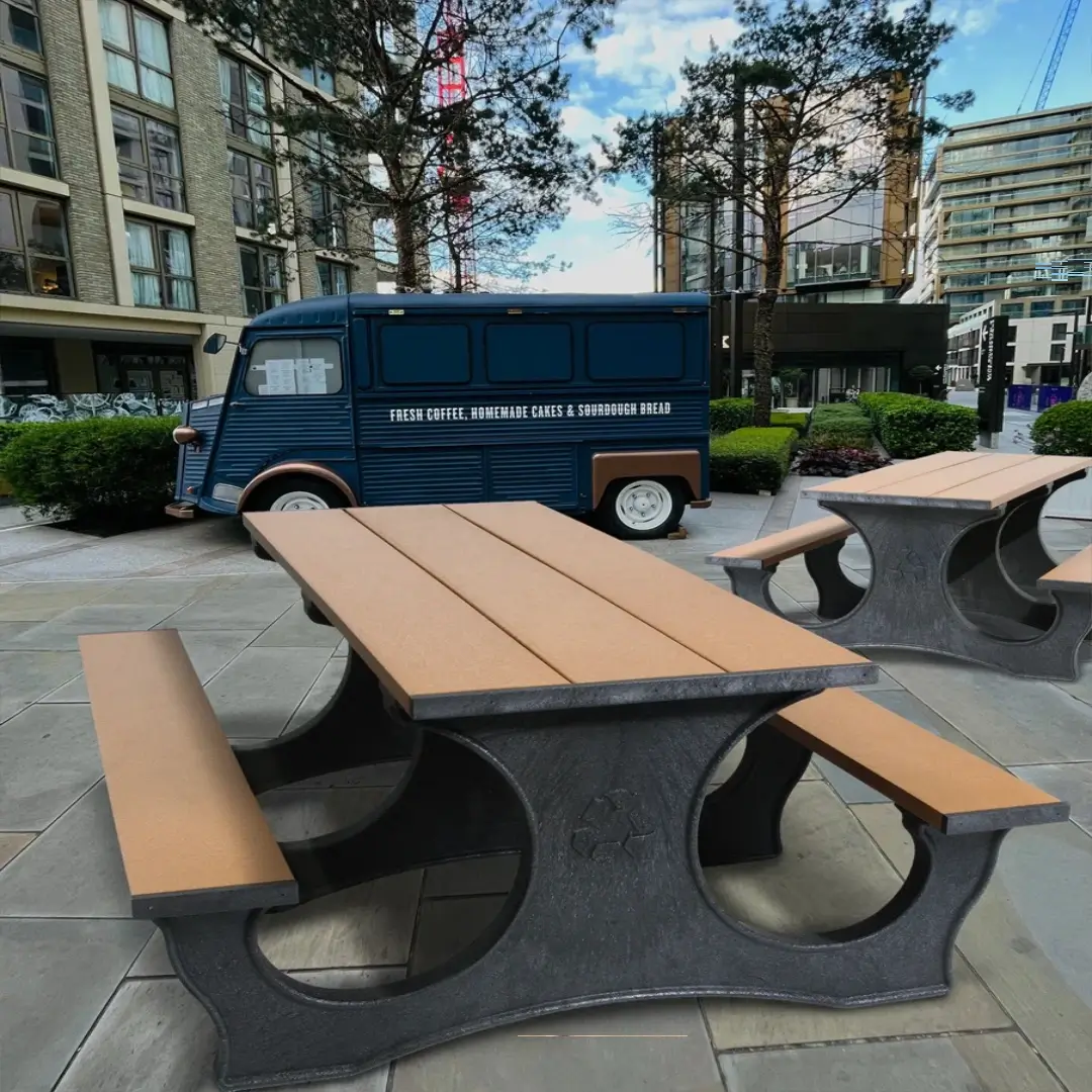 Commercial recycled plastic picnic tables with tan tops and black frames in an urban courtyard beside a mobile coffee truck.